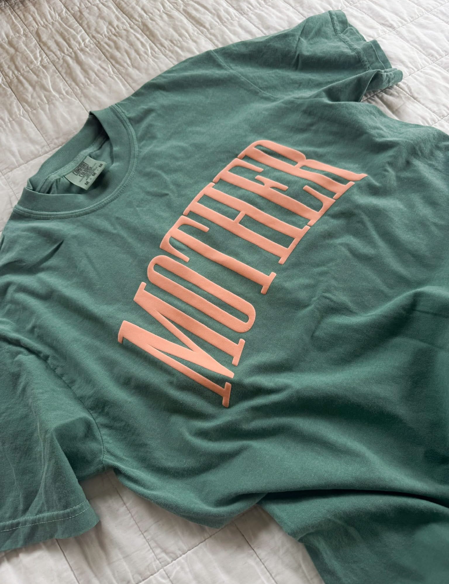 Light green adult comfort colors tee with coral 'mother' puff print across the front, seen on flat lay - Little Mama Shirt Shop