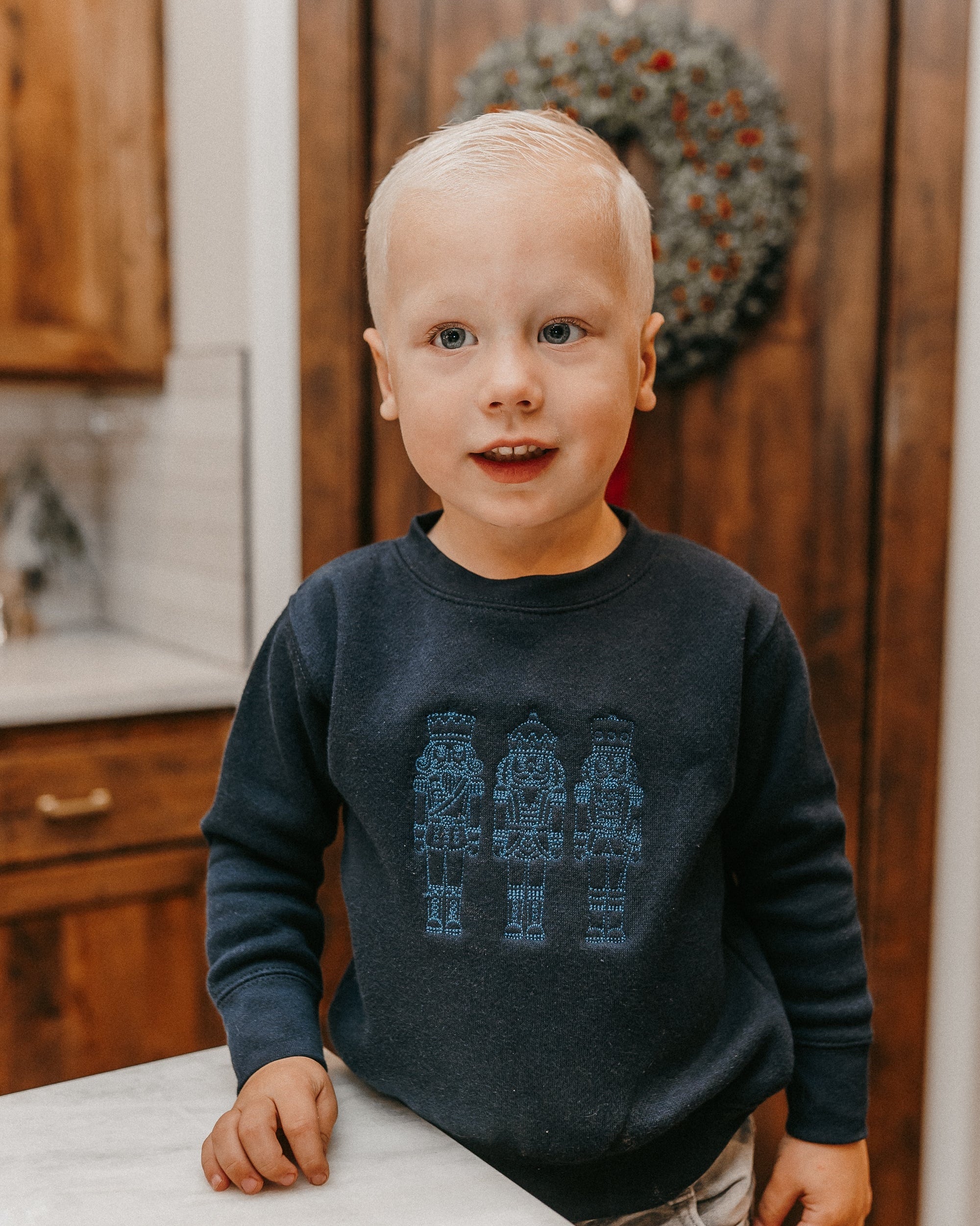 Child sweater in navy with 3 embroidered nutcrackers on chest, shown on model – Little Mama Shirt Shop