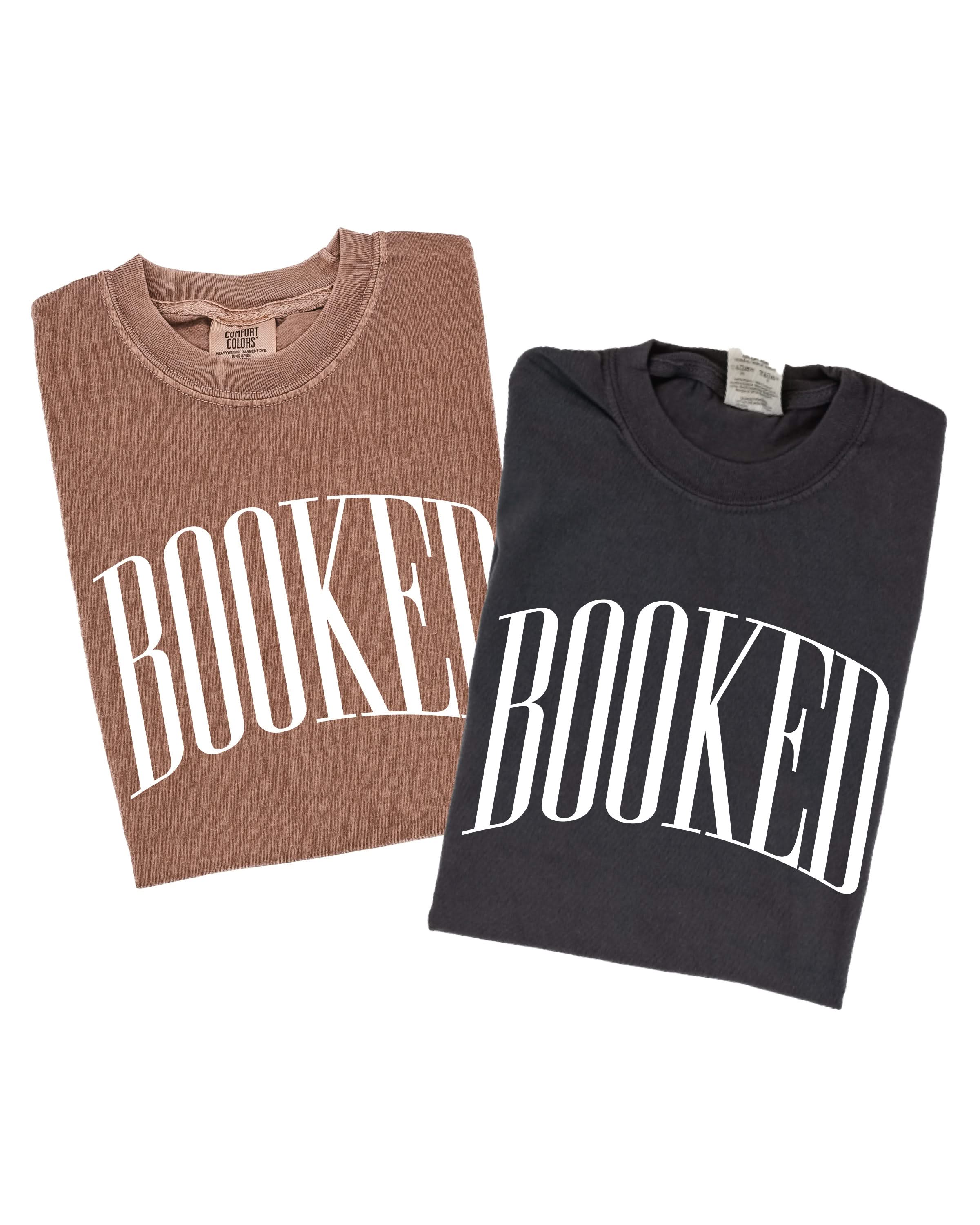 2 comfort colors tees in espresso and pepper with 'BOOKED' graphic on chest, shown on flat lay – Little Mama Shirt Shop